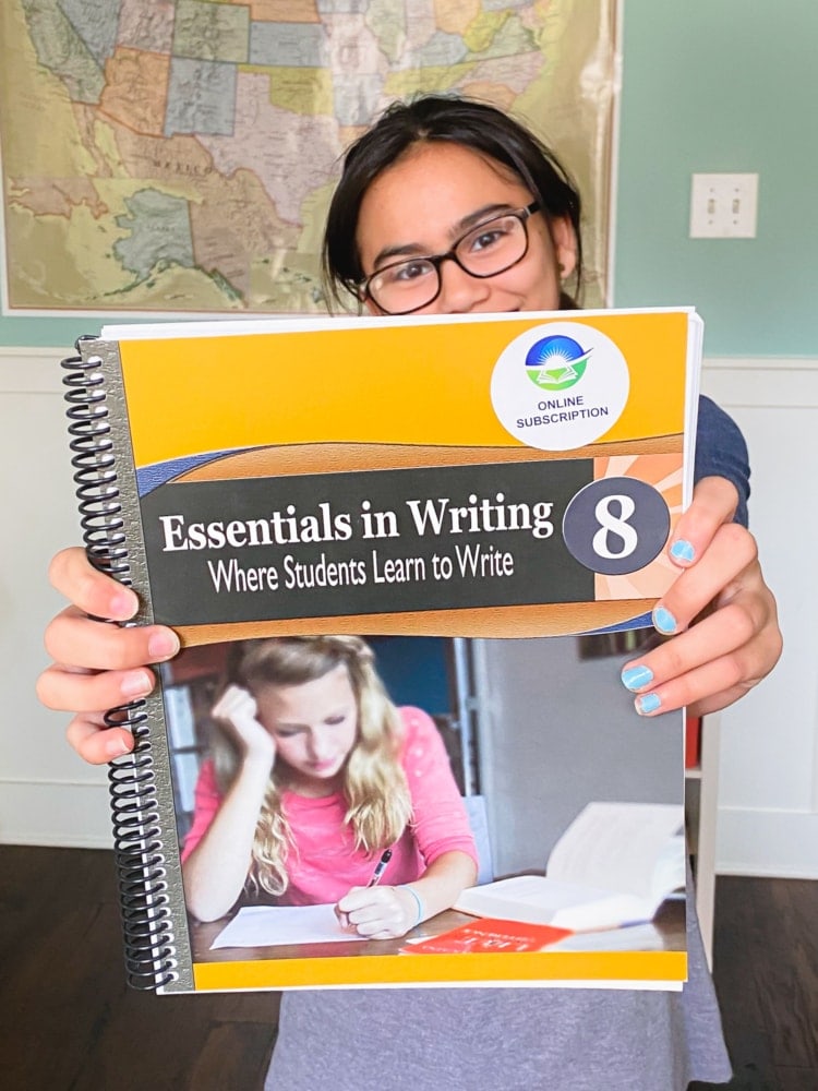 a girl holding essentials in writing level 8 workbook out in front of her