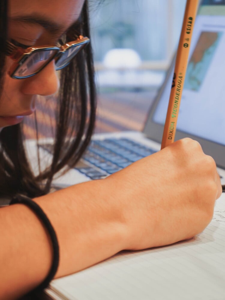 sitting at the kitchen island, our daughter writes out math problems in her notebook using a pencil as we start our first year homeschooling a middle schooler