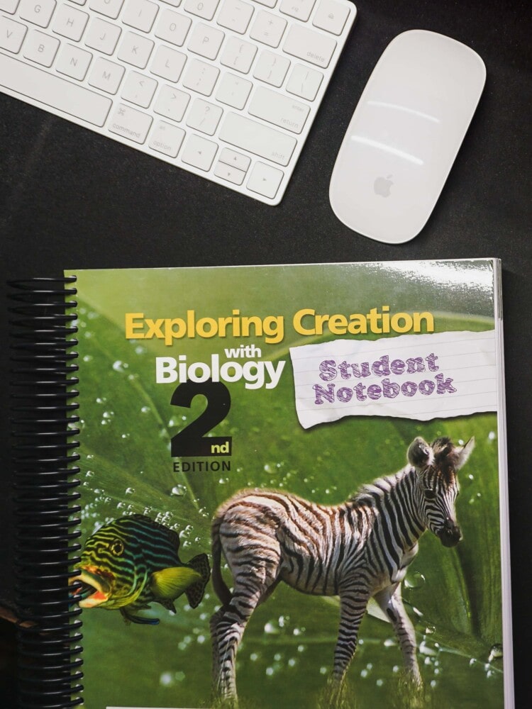 materials for a homeschool science curriculum for high school sitting on a desk, including the exploring creation student notebook for biology from apologia