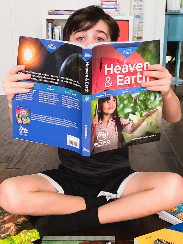 a boy sitting on the floor covering half his face with the book god's design for heaven an earth