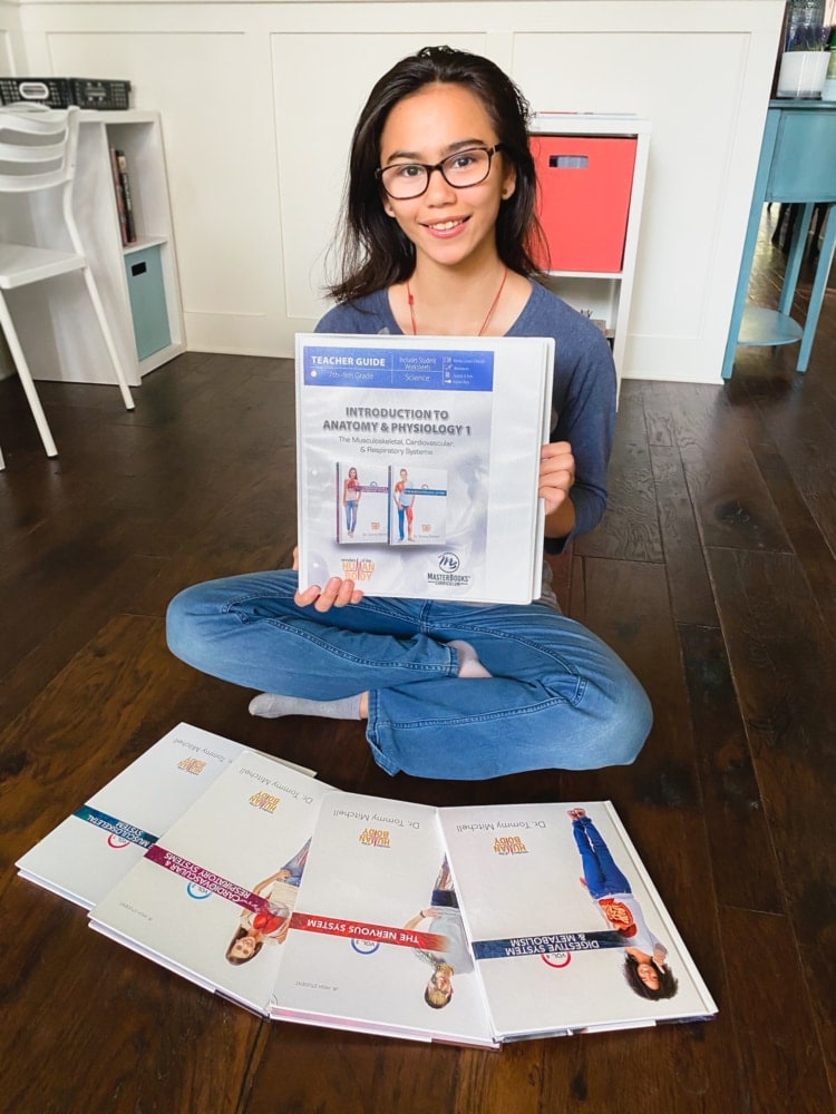 a girl sitting on the floor holding a folder for introduction to anatomy and physiology and more books around her on the floor