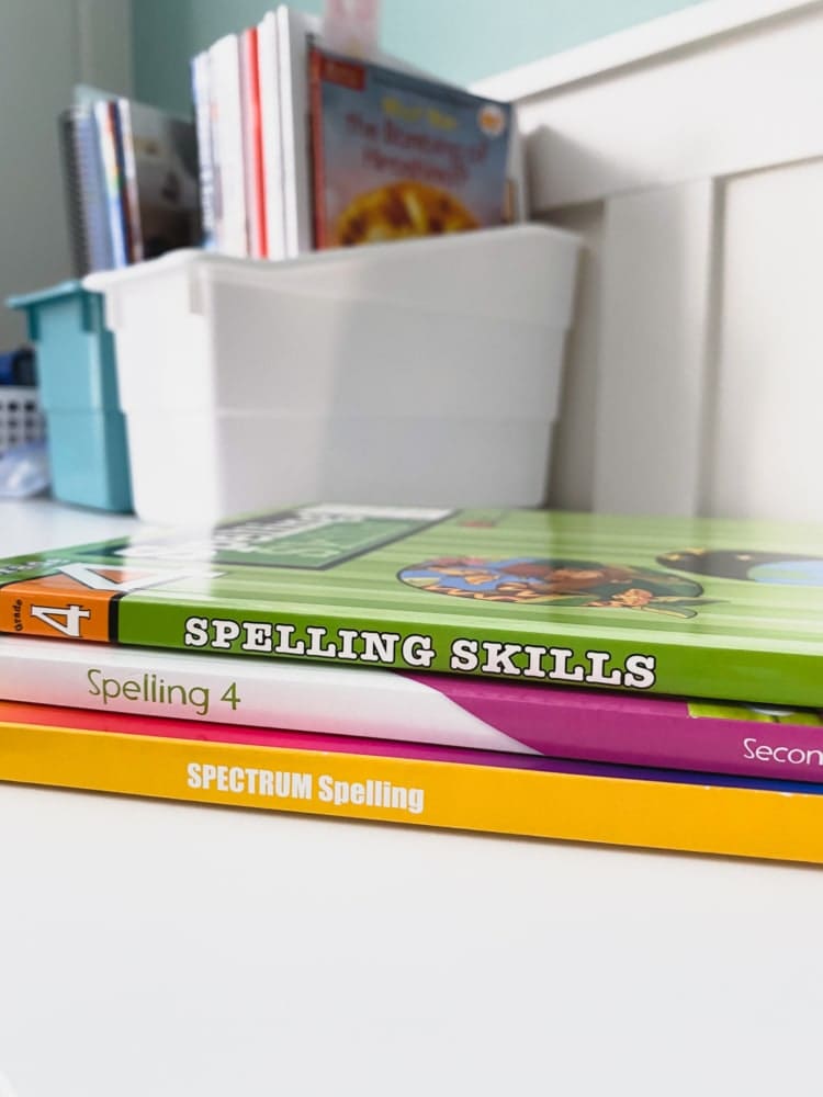 3 stacked spelling workbooks with more books in the background