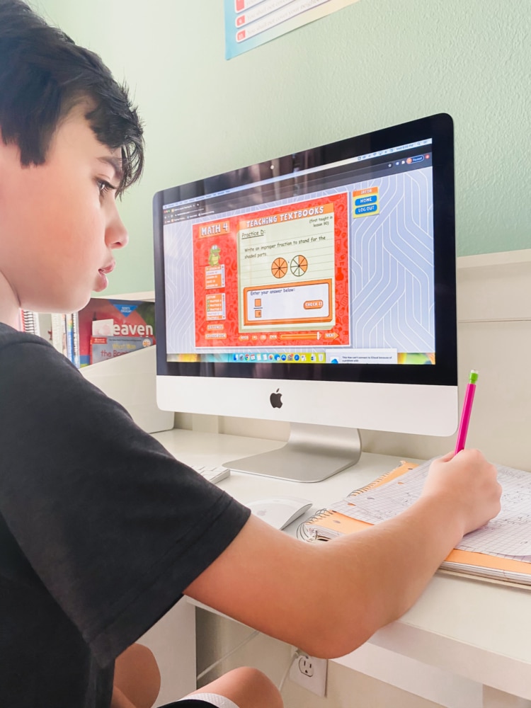 boy sitting in front of computer monitor working on math program teaching textbooks