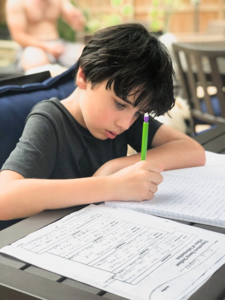 boy doing school work outside on a patio table