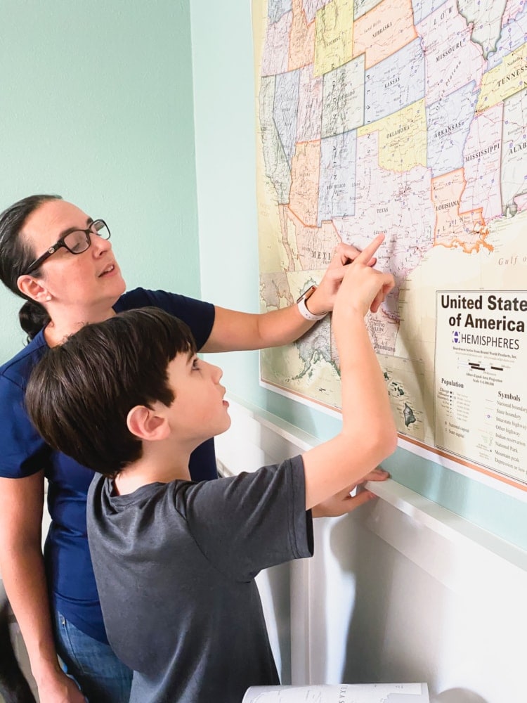 a woman and a boy pointing to Texas on a map on the wall