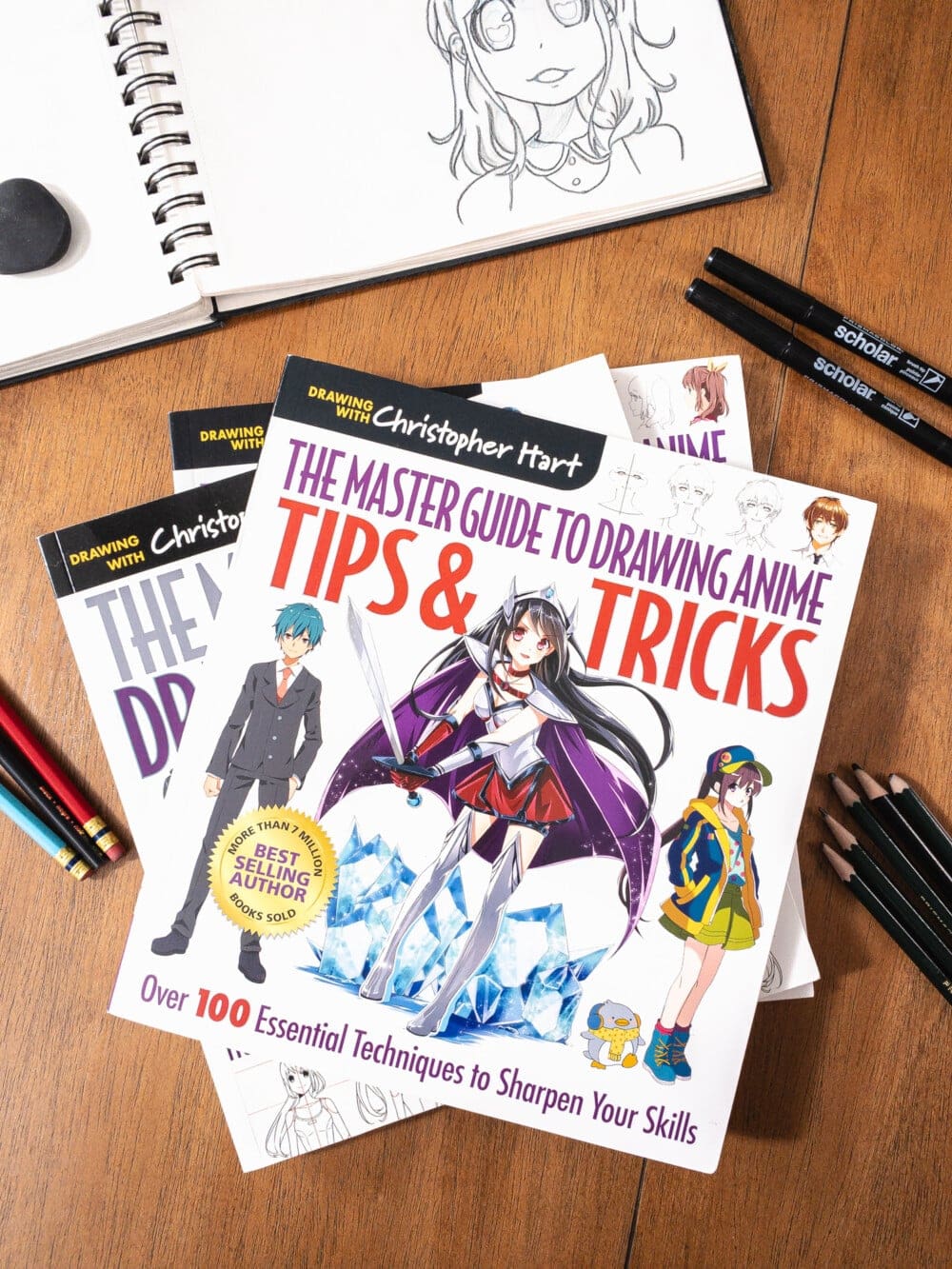 the master guide to drawing anime by christopher hart stacked on a table with other art guides, a sketchbook, and some drawing pencils