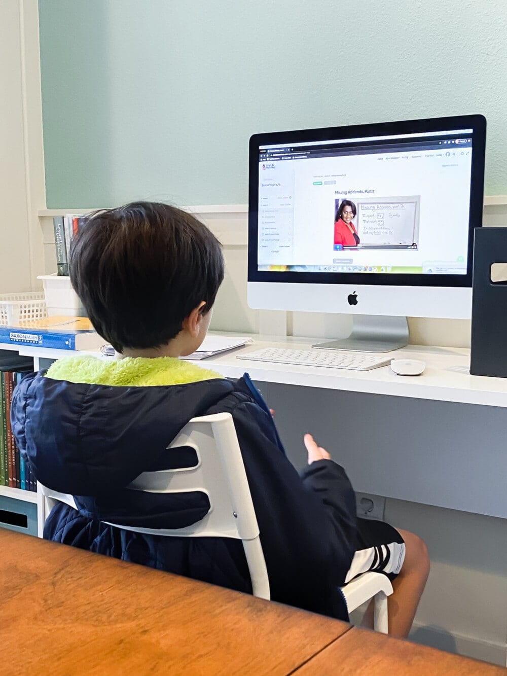 a child sitting in a chair at a desk watching online video math lessons for the saxon math 5/4 homeschool curriculum on a desktop computer